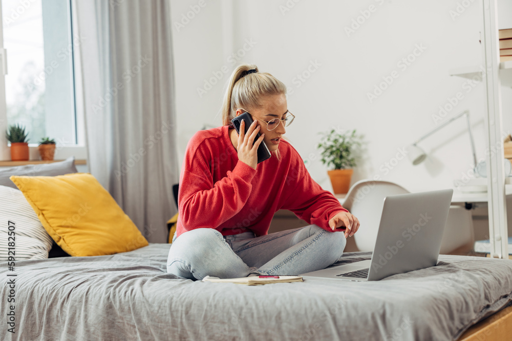 A young Caucasian woman is talking on the phone and sitting on the bed A young Caucasian woman is talking on the phone and sitting on the bed