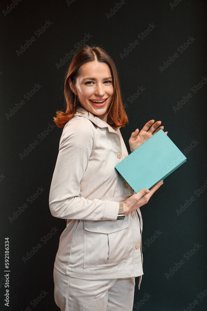 Holding blue box. Young woman with aligner is standing against black background
