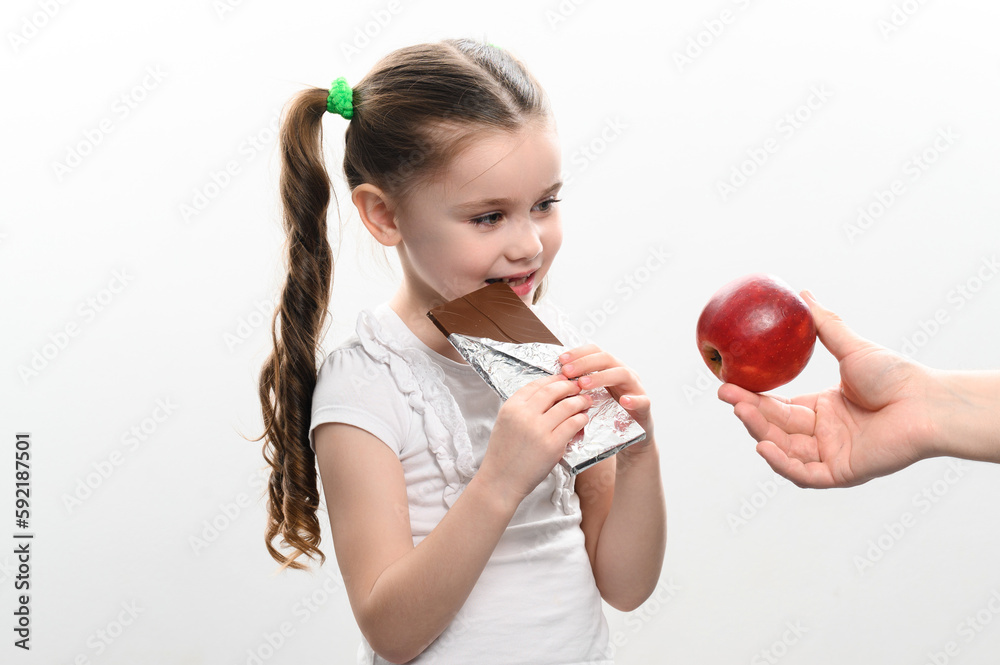 Portrait of a little girl on a white background, she chooses chocolate instead of an apple. Portrait of a little girl on a white background, she chooses chocolate instead of an apple.