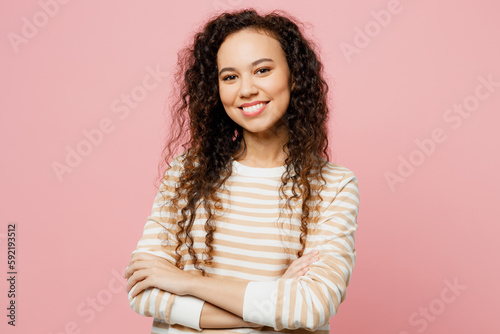 Young smiling happy fun confident woman of African American ethnicity she wearing light casual clothes hold hands crossed folded look camera isolated on plain pastel pink background studio portrait.