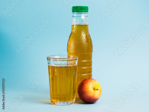 Apple juice drink in plastic bottle and reusable glass cup on blue paper background. Concept of earth day, zero waste and plastic recycling.