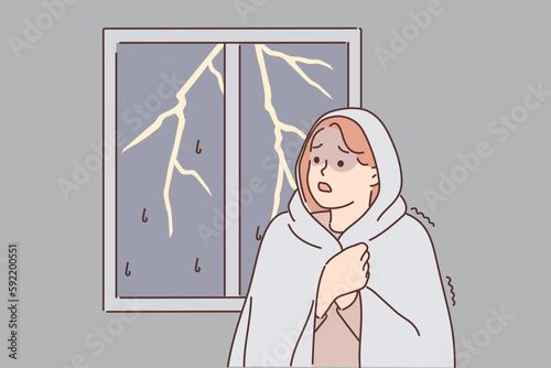 Woman was frightened by lightning and storm outside window wrapped herself in blanket