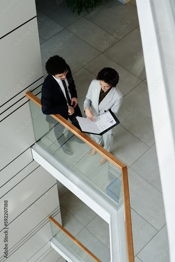 High angle view of young business colleagues discusing documents together standing in office hall