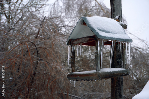 Feeder for birds and forest animals, covered with a layer of ice, hanging icicles on the edges of the roof. Winter white snow, selective focus © Алексей Максимов