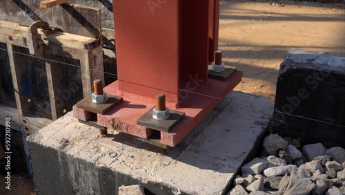 Metal supporting column mounted on the base pedestal  with huge nuts on screw rods on a building site.