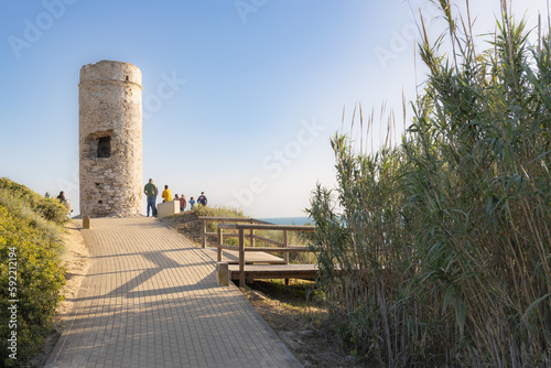 Torre vigía en una playa de Cádiz en San Fernando al atardecer con cielo despejado azul, con grupo de gente contemplando atardecer.