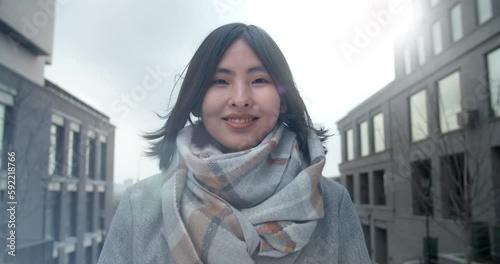 Asian woman stands between business buildings and looks at the camera. Winter sun. lens flares.