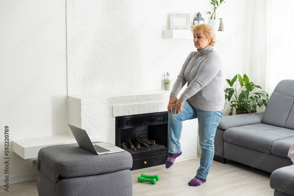 Home Sport. Active Senior Woman Doing Warming Stretching Exercises In Front Of Laptop, Training With Online Tutorials Home Sport. Active Senior Woman Doing Warming Stretching Exercises In Front Of Laptop, Training With Online Tutorials