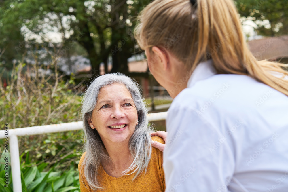 Female doctor consoling elderly woman in garden