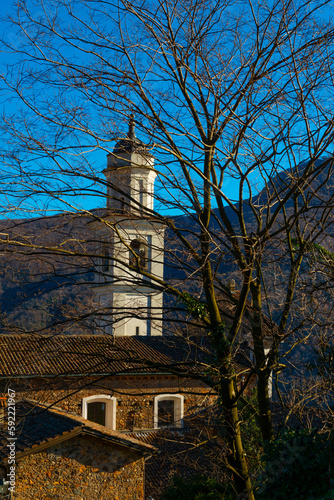 Church of Saints Fedele and Simone and Bare Tree with Mountain in a Sunny Day in Vico Morcote, Ticino in Switzerland.