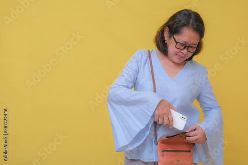 A middle-aged Asian woman took out her cell phone from her sling bag. photo