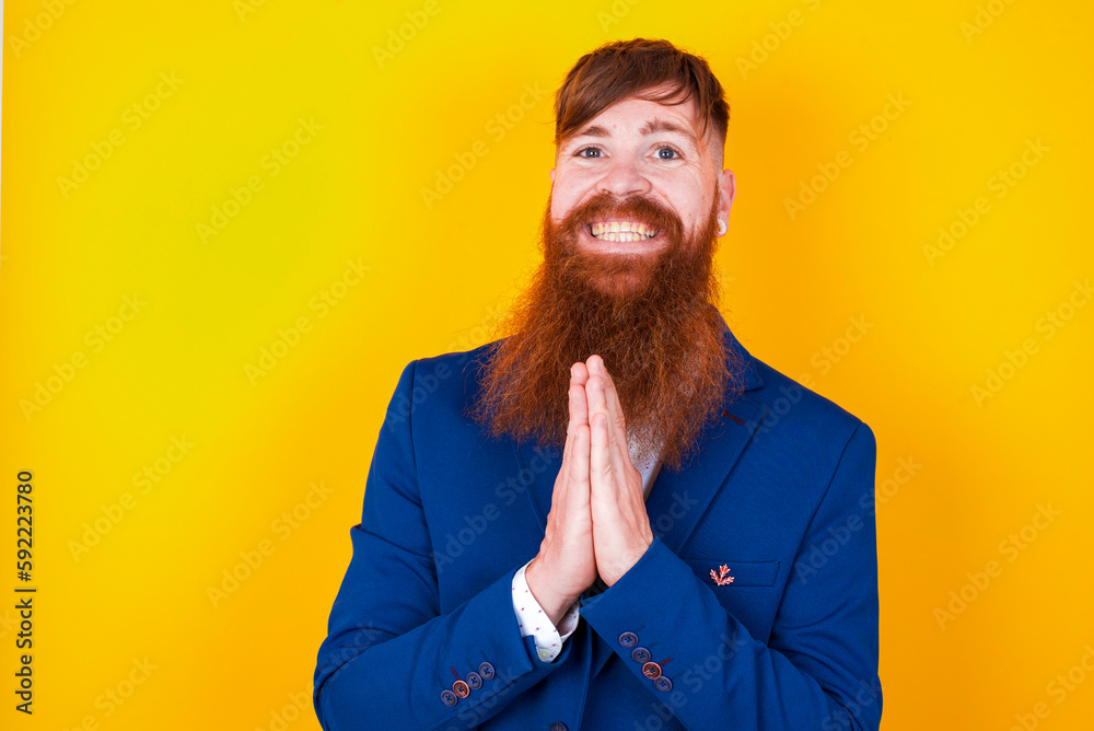 red haired man wearing blue suit over yellow studio background praying with hands together asking for forgiveness smiling confident. red haired man wearing blue suit over yellow studio background praying with hands together asking for forgiveness smiling confident.