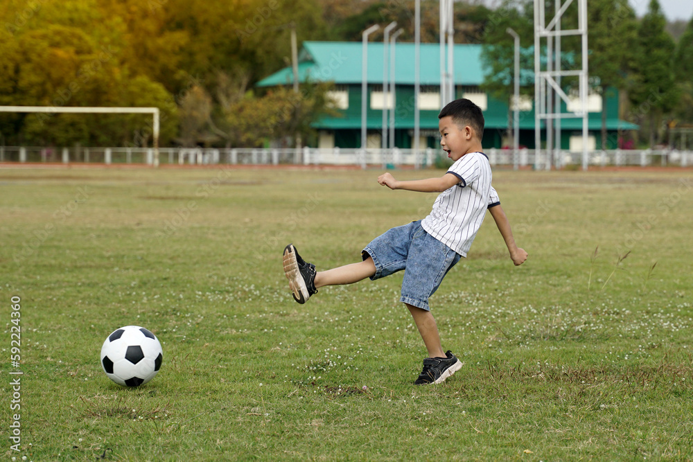 Asian boy kicking ball in soccer field. Concept. outdoor activity, sport, playground, leisure activity. Soft and selective focus.  