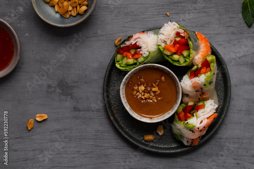 Summer rolls with fresh vegetables and shrimps or prawns and peanut and chili sauce on dark grey background. Vietnamese appetizer. Top view. Healthy food concept