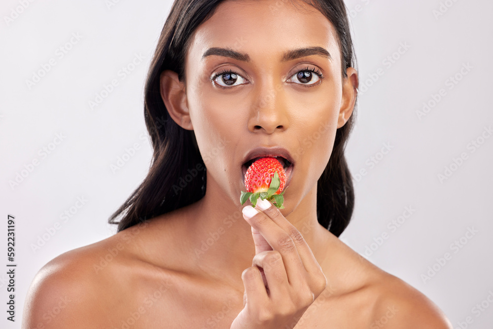 Portrait, skincare and a woman biting a strawberry in studio on a gray background for health, diet or nutrition. Face, beauty and serious with an attractive young female model eating a fruit berry Portrait, skincare and a woman biting a strawberry in studio on a gray background for health, diet or nutrition. Face, beauty and serious with an attractive young female model eating a fruit berry