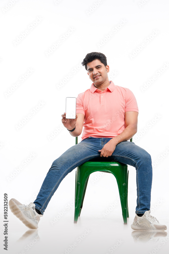 Handsome and stylish indian man sitting on chair and showing smartphone screen. Handsome and stylish indian man sitting on chair and showing smartphone screen.