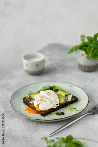 Healthy Breakfast with Bread Toast and Poached Egg with Avocado and cream cheese on a light grey background.