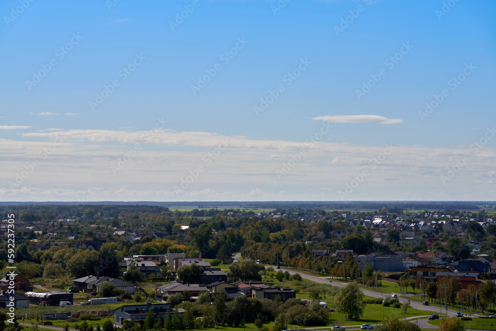 High-angle shot of the city Panevezys suburbs with green trees, blue sky and clouds background