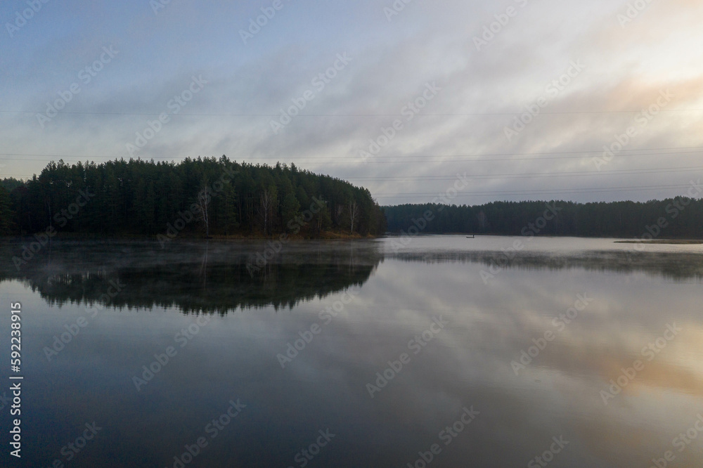 Fototapeta premium Drone photography of lake, lakeside and fog and fishing man in a boat during summer sunset.