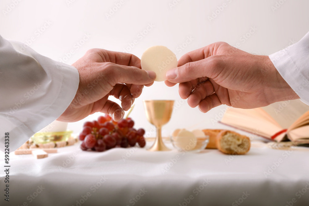 Priest consecrating a host with table with sacred objects behind Priest consecrating a host with table with sacred objects behind