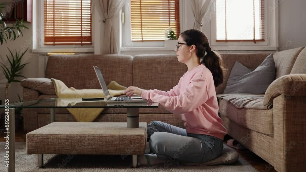 Freelance and remote work. Side view of young caucasian woman working on laptop, sitting on floor near sofa. Sucessful student learning in home. Freelance and remote work. Side view of young caucasian woman working on laptop, sitting on floor near sofa. Sucessful student learning in home.