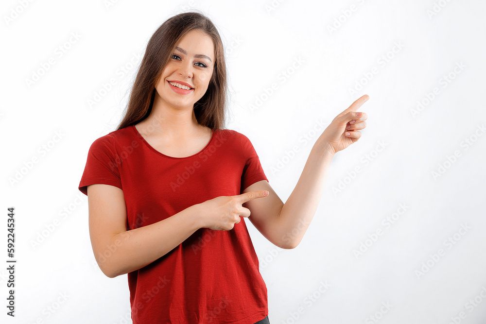 Smiling lovely girl points right at promo banner, shows advertisement on blank white space. Young brunette female looking happy by promotion offer, stands over white background Smiling lovely girl points right at promo banner, shows advertisement on blank white space. Young brunette female looking happy by promotion offer, stands over white background