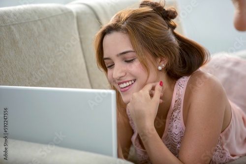 Woman lying on sofa and looking at laptop with smile photo