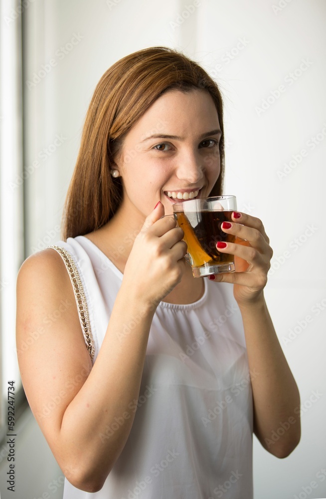 Woman holding glass of tea and looking at camera with smile in white background Woman holding glass of tea and looking at camera with smile in white background