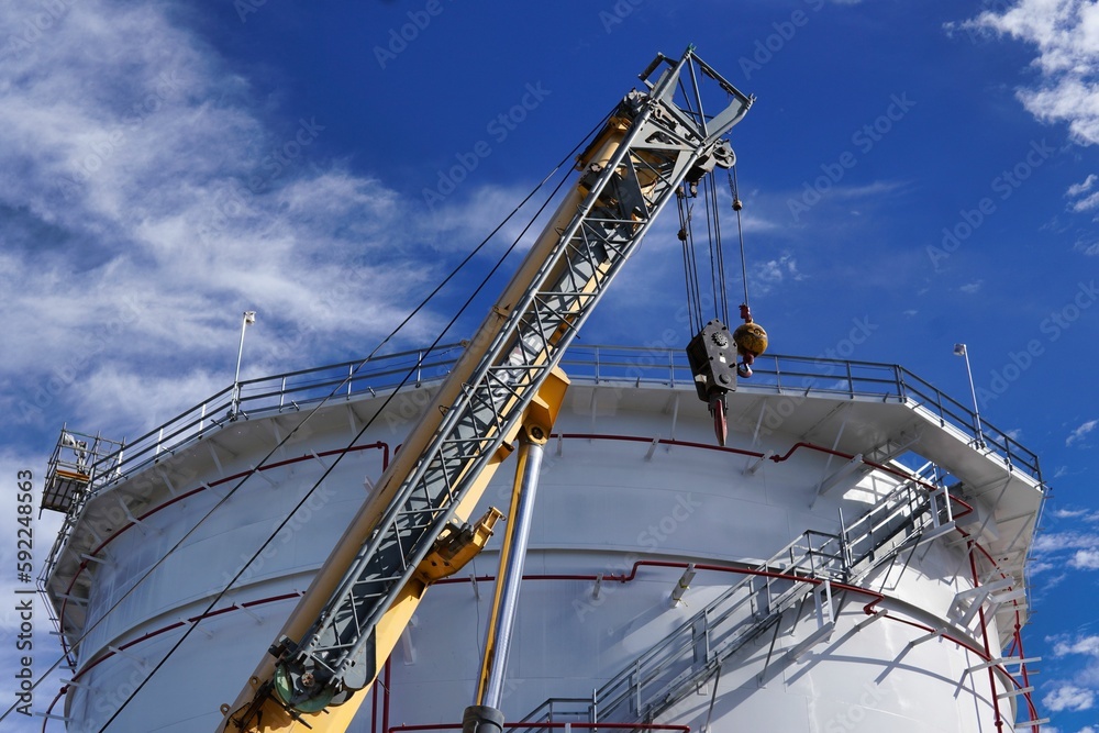 Metal crane near a huge oil energy tank under a blue cloudy sky Metal crane near a huge oil energy tank under a blue cloudy sky