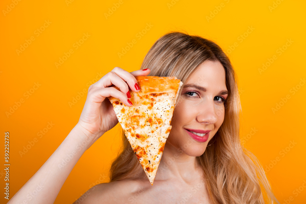 A beautiful fit young blonde girl posing with a pizza slice. Isolated on yellow.