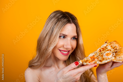A beautiful fit young blonde girl posing with a pizza slice. Isolated on yellow.