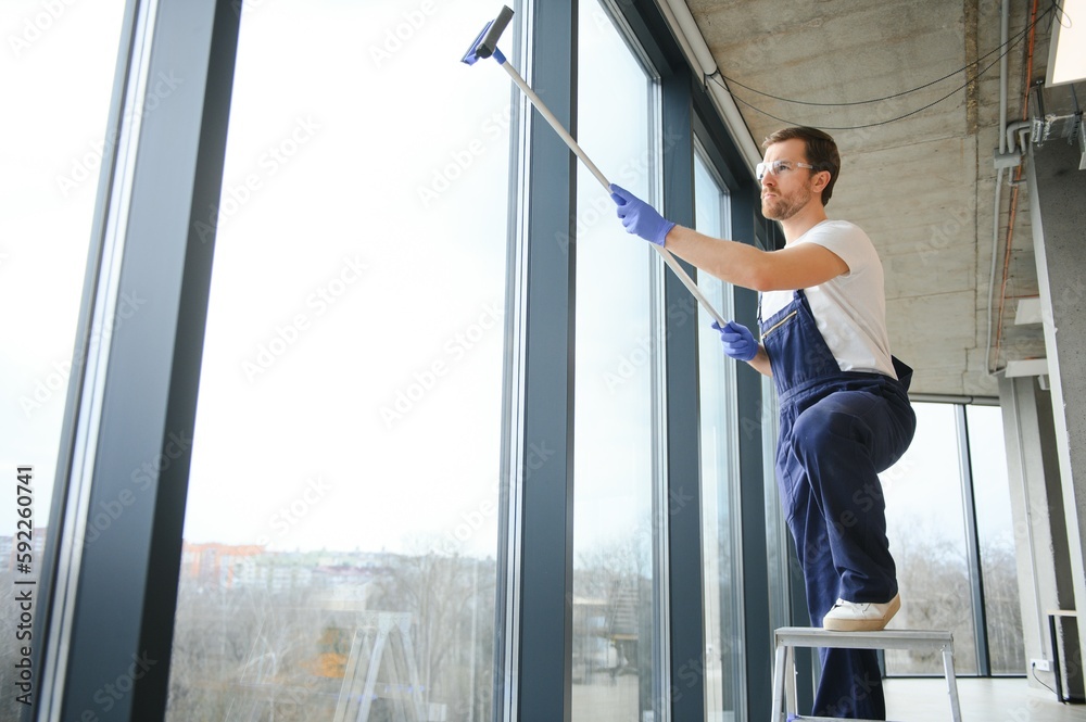 Fototapeta premium Male professional cleaning service worker in overalls cleans the windows and shop windows of a store with special equipment.