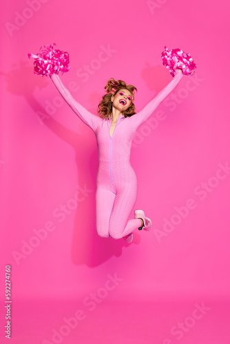 One young beautiful blond girl wearing sport suit jumping over pink studio background. Cheerleading club