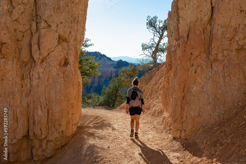 Rear view of woman hiking through steep cliffs of unique sandstone rock formations on Navajo trail in Bryce Canyon National Park, Utah, USA. Hoodoos (spire of sedimentary rock) in natural amphitheatre