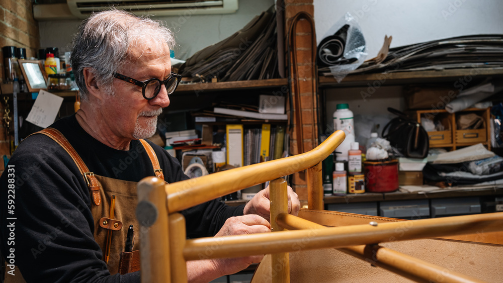 tanner gluing the leather parts to a chair made by hand in a small shop in rome center. traditional work tanner gluing the leather parts to a chair made by hand in a small shop in rome center. traditional work