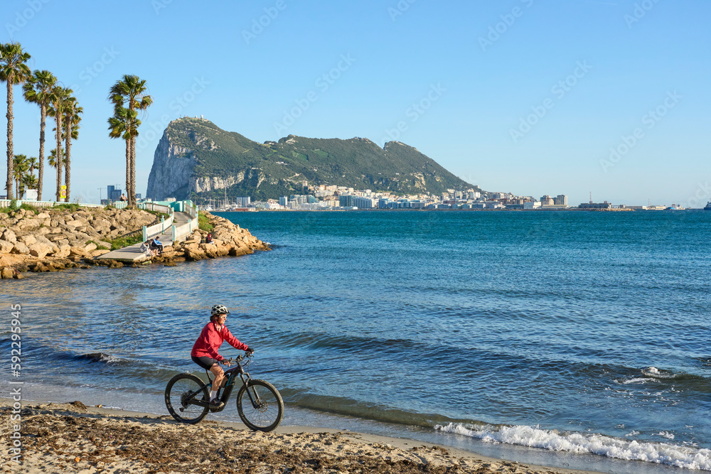 Fototapeta premium happy senior woman cycling with her electric mountain bike below the Rock of Gibraltar, Andalusia, Spain