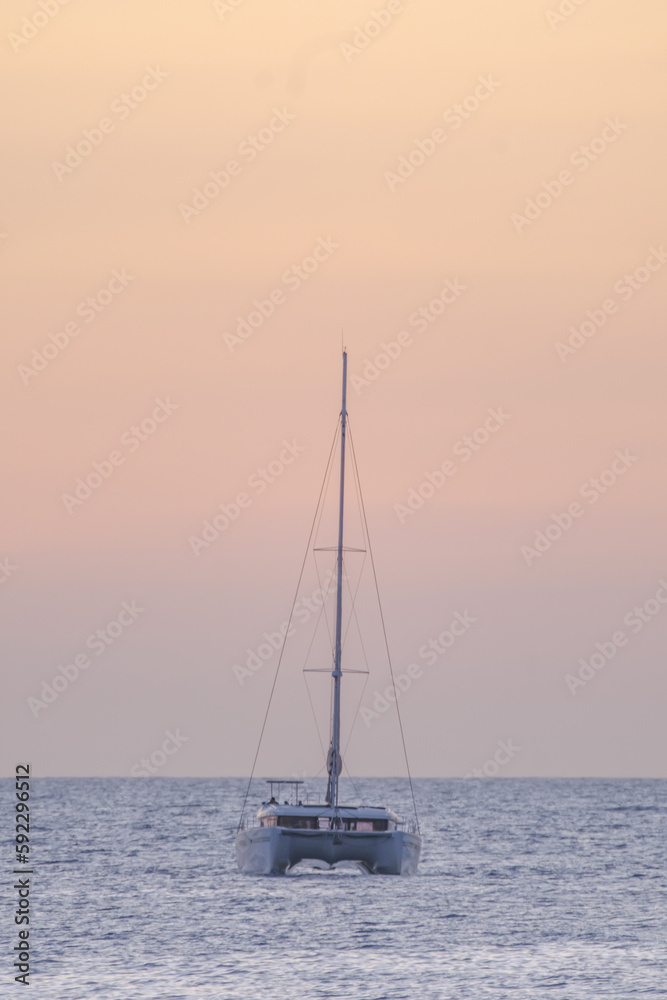 Sailboat on the ocean near the beach at sunset.