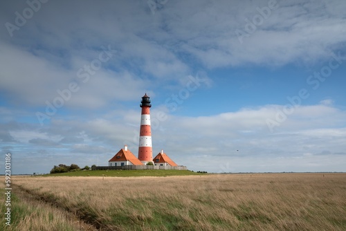Grass field with a lighthouse and houses in Westerhever  Germany and a cloudy sky in the background.