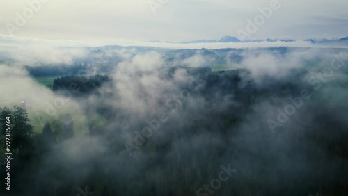 Impressive drone shot of the foggy Upper Austrian alpine foothills with Traunstein mountain in the background. Camera moves backwards through the patches of fog.