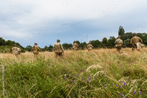 Historical reconstruction. World War II american infantry  soldiers  patrol the area  in the tall grass. View from the back.  Porąbka, Poland photo