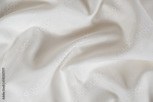 Satin crumpled fabric of light milky color, top view. Natural bed linen, sheets, abstract background of luxury fabric, wavy folds