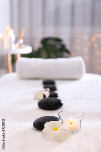 Close up shot of black volcanic stones laid in line and a rolled towel on the massage table in a spa salon room. Bokeh lights on the background. Copy space.