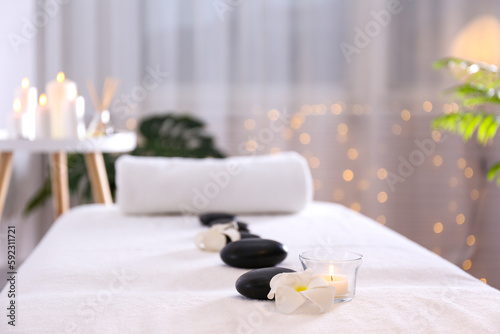 Close up shot of black volcanic stones laid in line and a rolled towel on the massage table in a spa salon room. Bokeh lights on the background. Copy space. © Evrymmnt