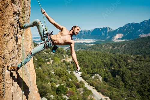 Fit body handsome man rock climber looking away on height vertical rock with rope. Amazing nature view on background