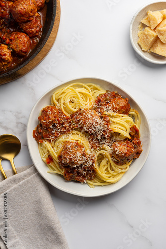 Cooking of Italian pasta with tomato vegetable sauce, meatballs, sprinkled with cheese. Spaghetti with parmesan in a plate on a marble table with ingredients and cutlery. View from above.