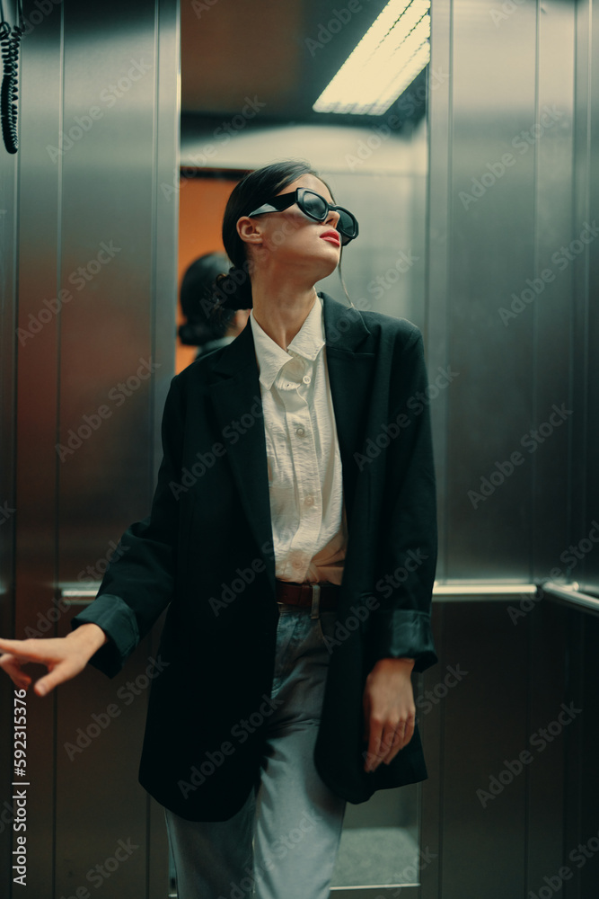 Stylish woman in black jacket and sunglasses posing in elevator, fashion model Stylish woman in black jacket and sunglasses posing in elevator, fashion model