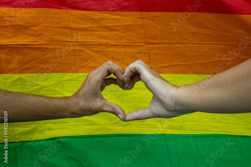 Human hands make heart shape in background of LGBT flag