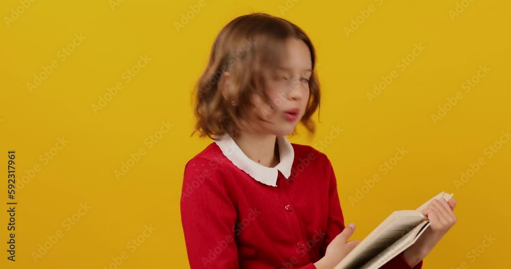 Happy schoolgirl reading a book on yellow studio background Happy schoolgirl reading a book on yellow studio background