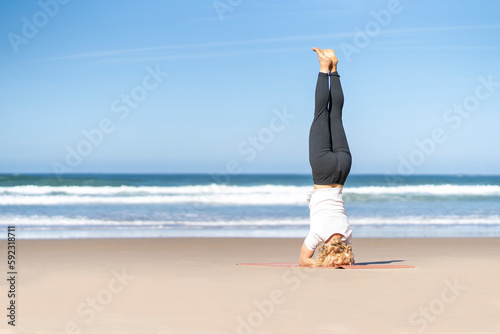 Girl doing yoga Salambha pose. Woman on supported headstand Salamba Sirsasana sirsa by the beach photo