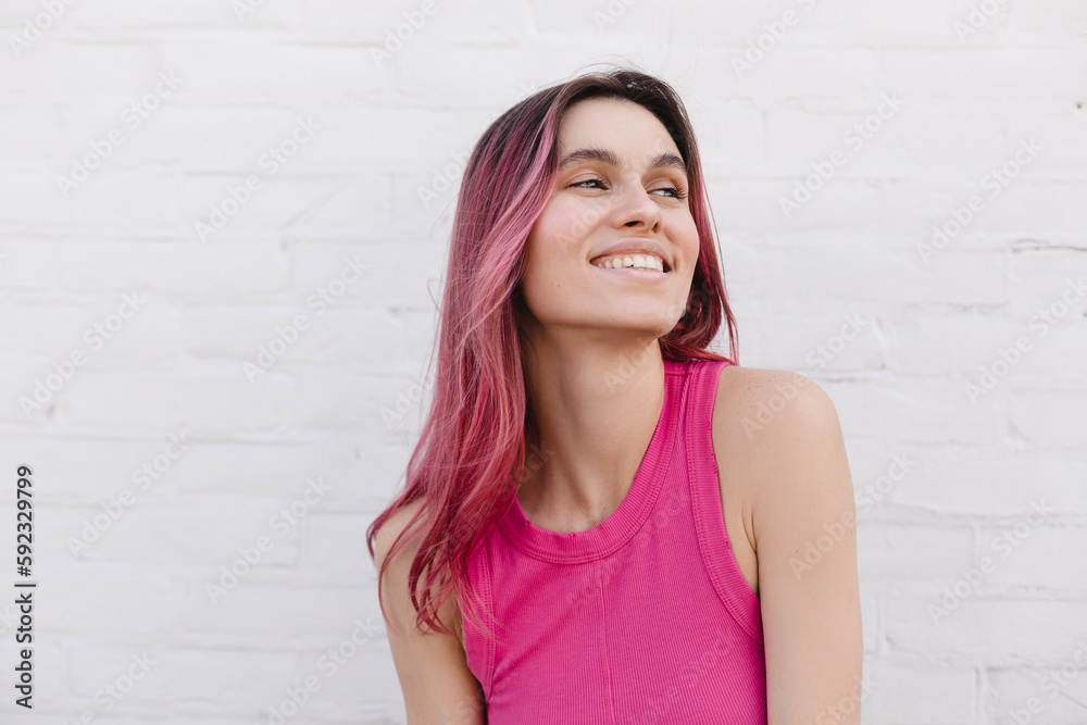 Positive pink hair woman in pink top. Portrait of happy attractive lady at background of white brick wall. Teeth smile woman look at side, flying hair on the wind. Positive pink hair woman in pink top. Portrait of happy attractive lady at background of white brick wall. Teeth smile woman look at side, flying hair on the wind.